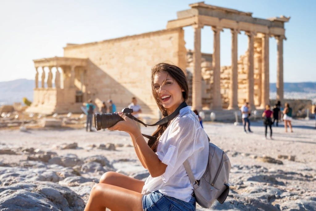 Woman carrying a camera with Partenon temple as backdrop