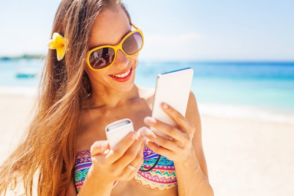 Woman on a beach looking at her phone with portable charger