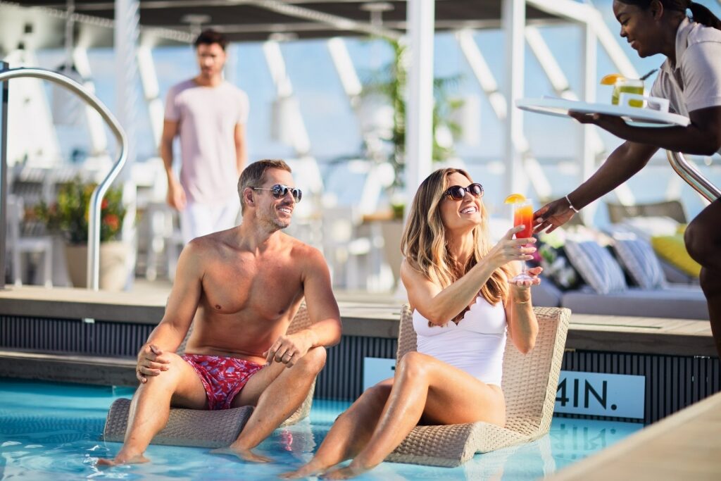 Couple hanging out by the pool while being served with drinks