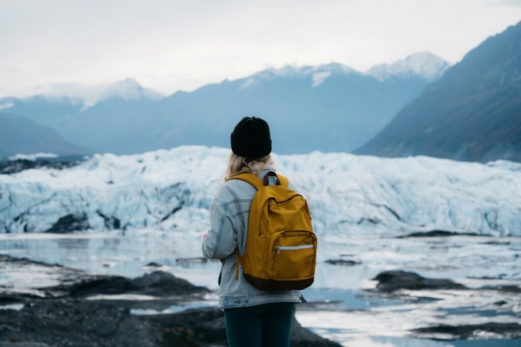 Woman carrying yellow backpack with icy backdrop in Alaska