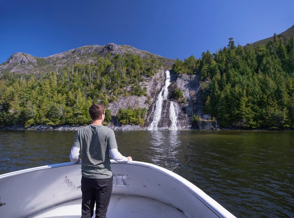 Man standing on a boat in front of waterfalls in Alaska