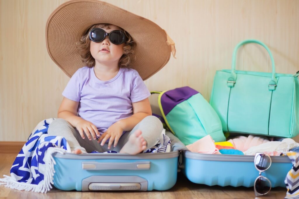 Toddler wearing hat and sunglasses sitting on a luggage