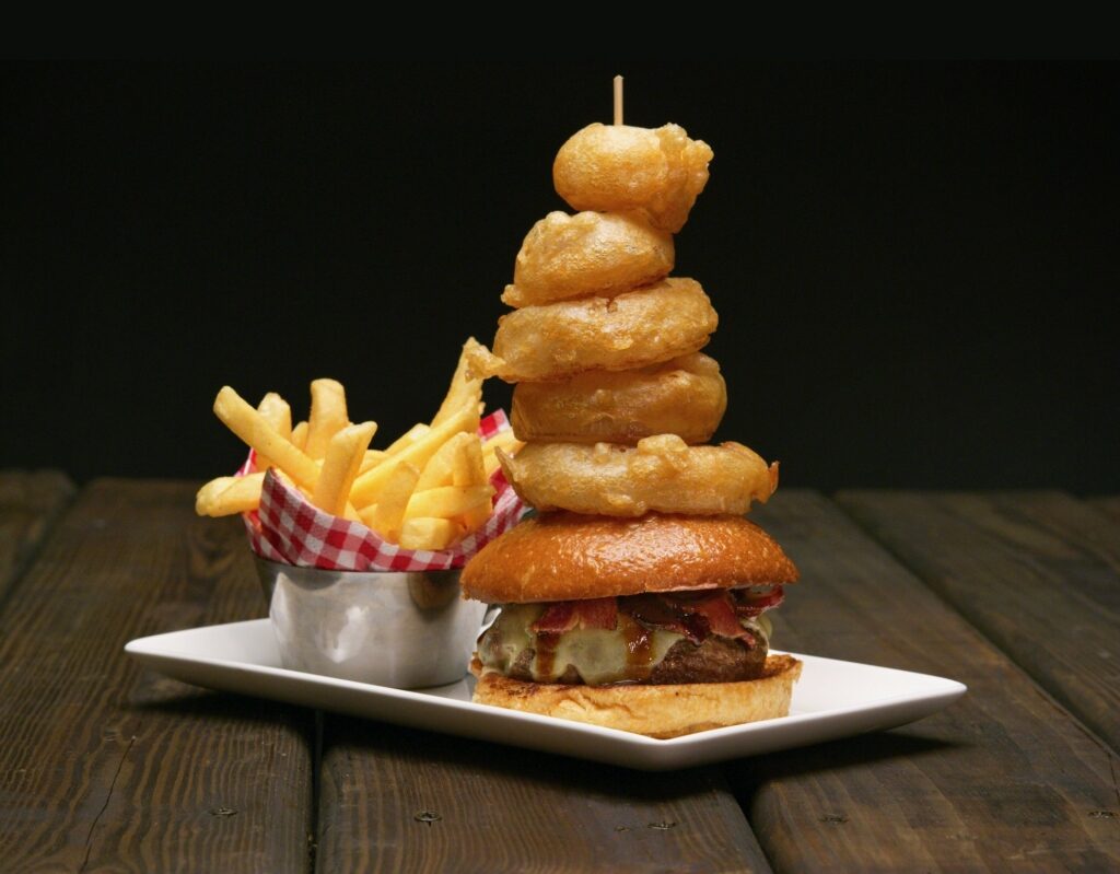 Cheeseburger topped with onion rings with fries on the side