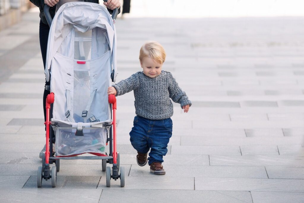 Toddler walking beside light stroller