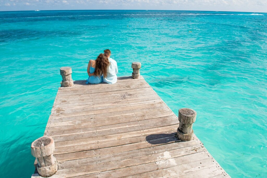 Couple sitting on a boardwalk surrounded by clear blue water