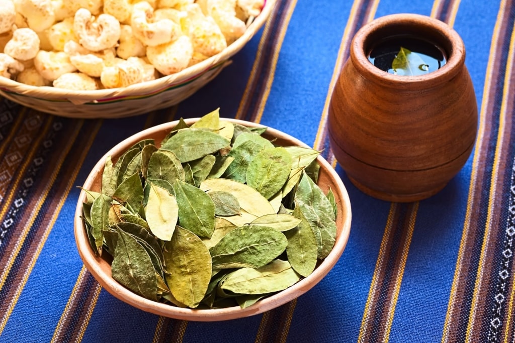 Bowl of coca tea leaves alongside a cup of tea