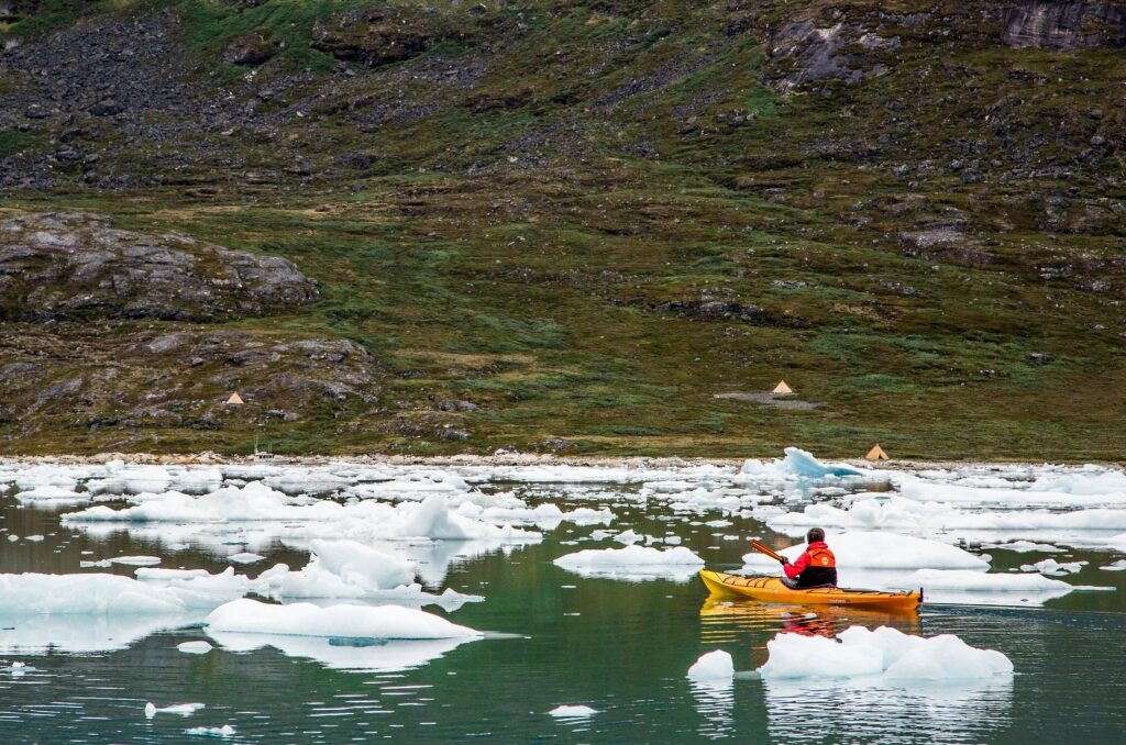 Woman kayaking in Greenland with icebergs floating around