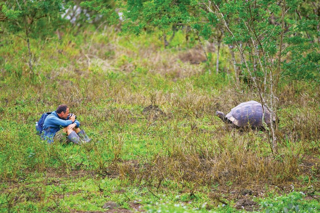 Man wearing rain gear while taking a photo of a Galapagos tortoise