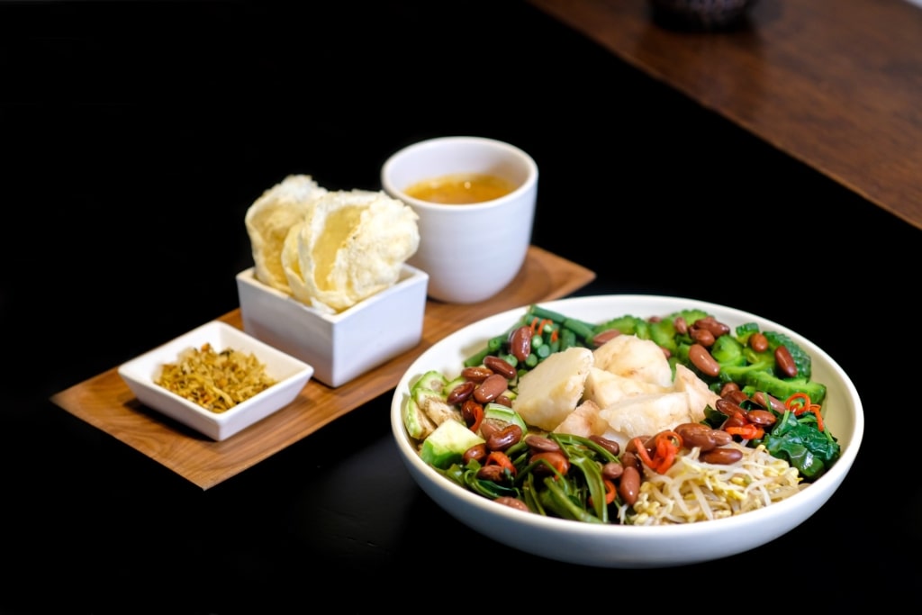 Bowl of Balinese vegetable salad dish serombotan served with peanut sauce on a wooden tray