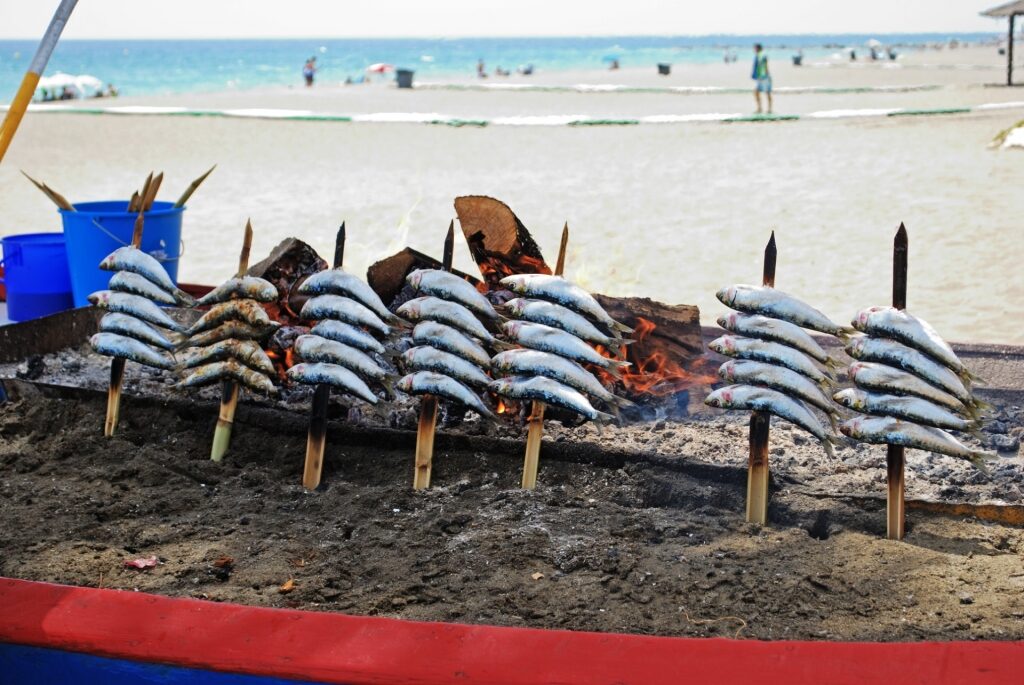 Sardines being cooked on a wooden skewer