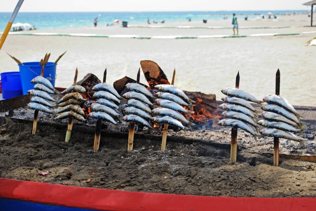 Sardines being cooked on a wooden skewer