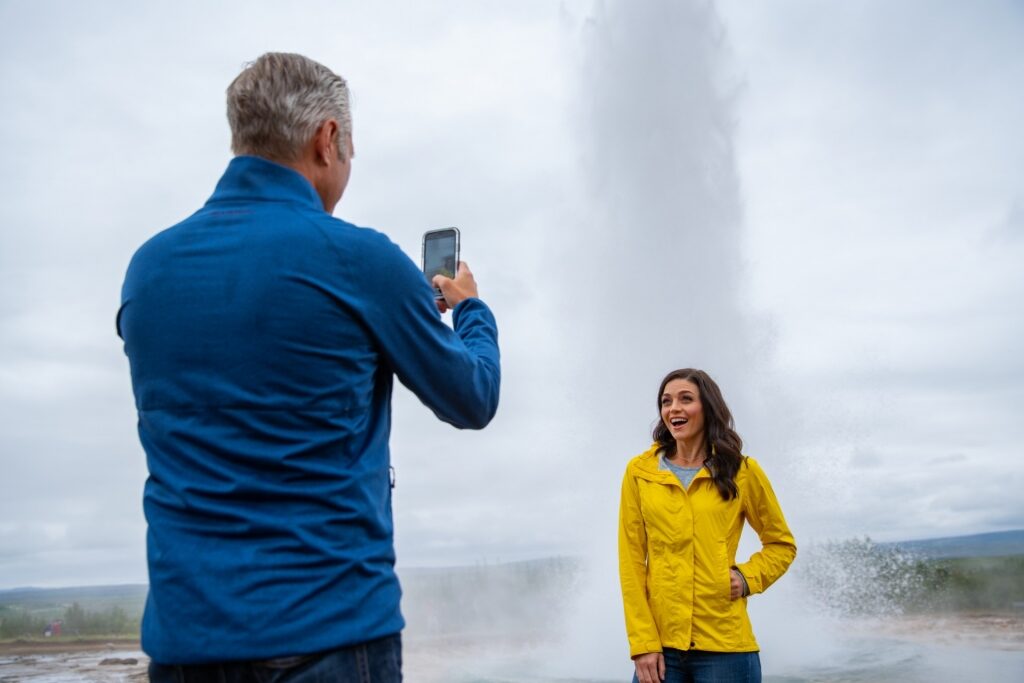 Couple taking a photo with Geysir Hot Springs as backdrop