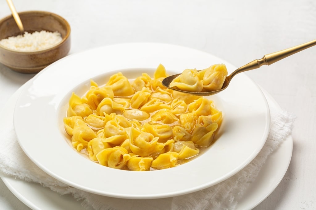 Person scooping a spoonful of tortellini in brodo