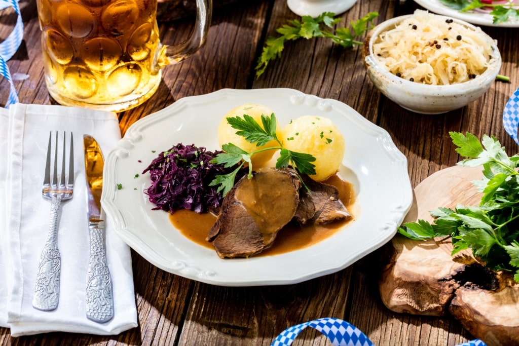 Sauerbraten meal with side dishes and beer on table, traditional food in Cologne