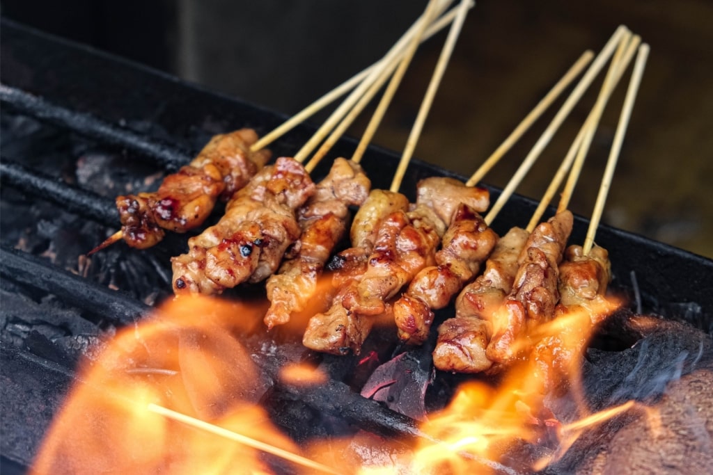 Juicy chicken satay skewers cooking over charcoal grill