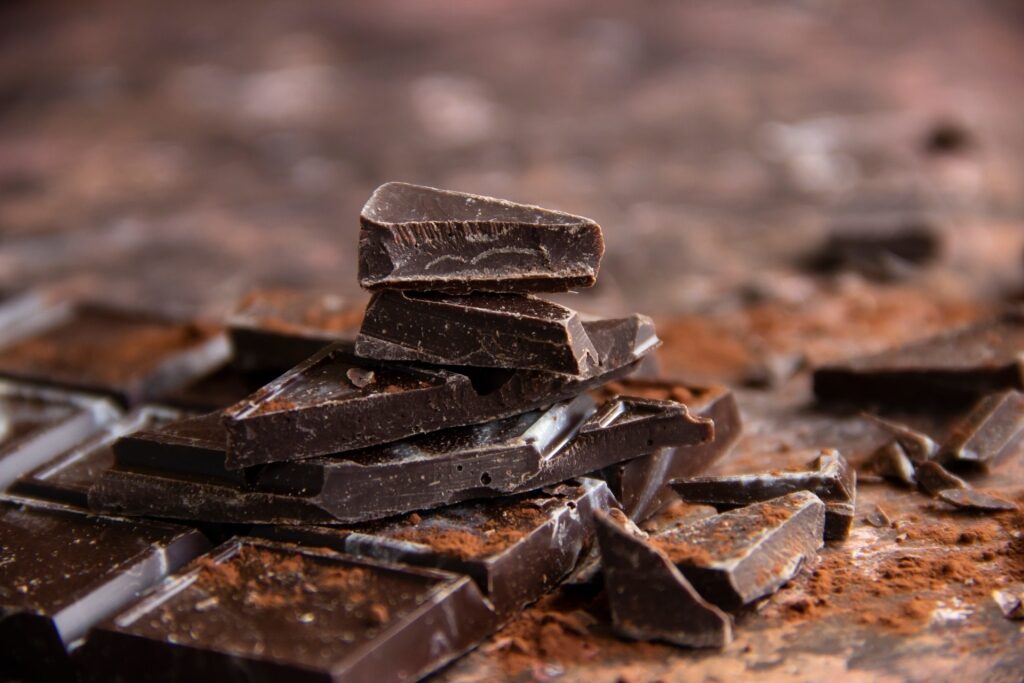 Close-up of dark chocolate bar with broken pieces and cocoa powder on brown background