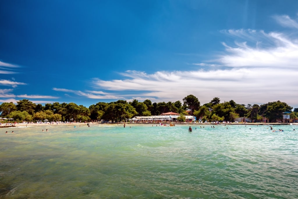 Tourists swimming and enjoying the clear blue waters at Borik Beach in Zadar, Croatia
