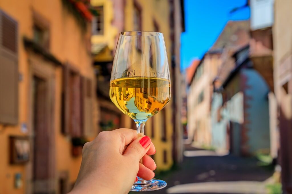 Woman’s hand holding a glass of Alsace wine at an outdoor restaurant