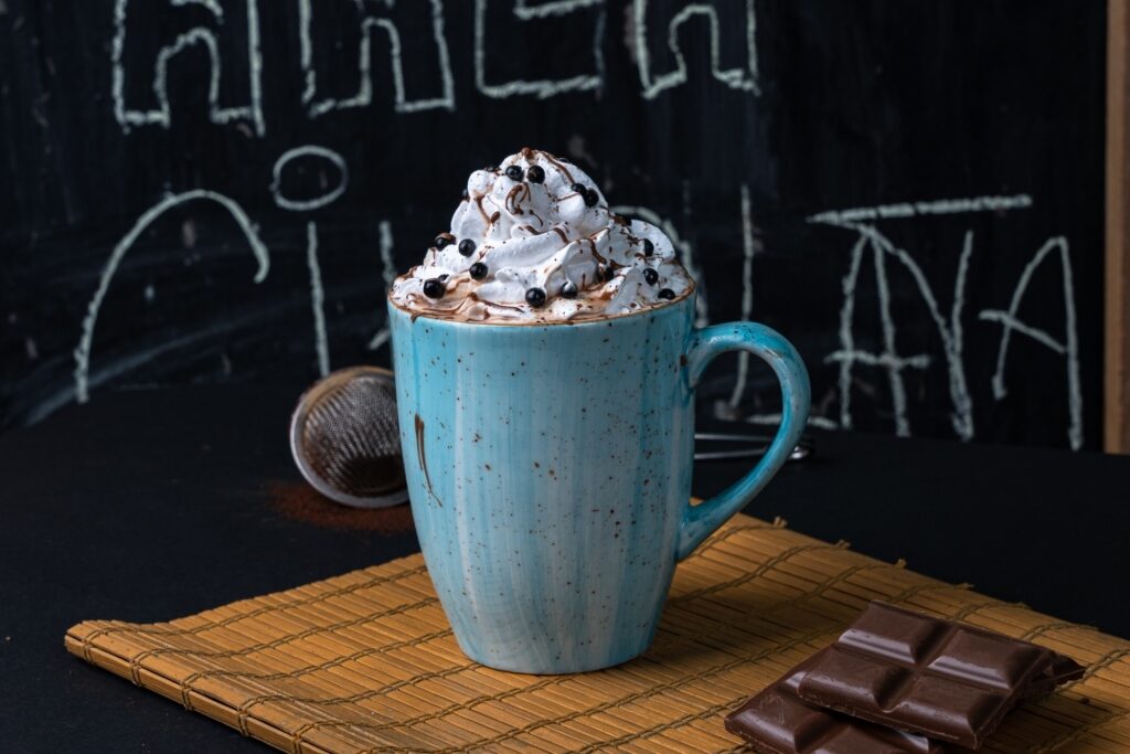 Hot chocolate in turquoise mug topped with whipped cream and chocolate balls on rustic black background