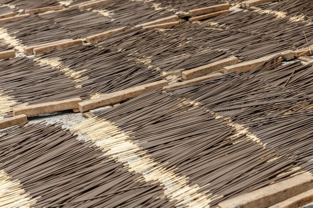 Rows of homemade incense sticks drying in the sun along the roadside