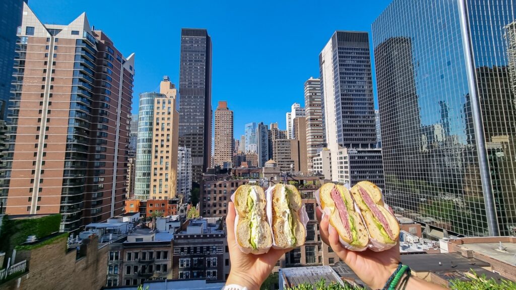 Two halved bagels held in hand with New York City skyline and skyscrapers in the background