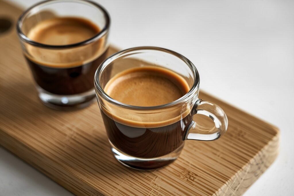 Pair of clear glass espresso shot glasses on a wooden board