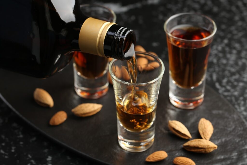 Amaretto liqueur pour alongside almonds on a black table