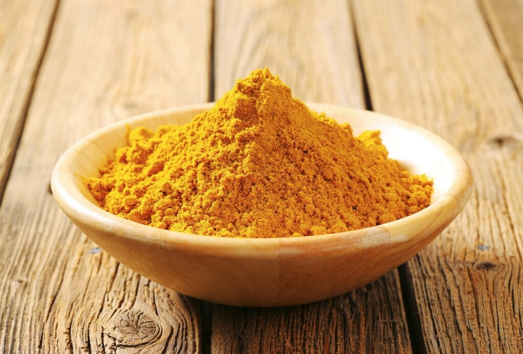 Wooden bowl filled with bright yellow curry powder