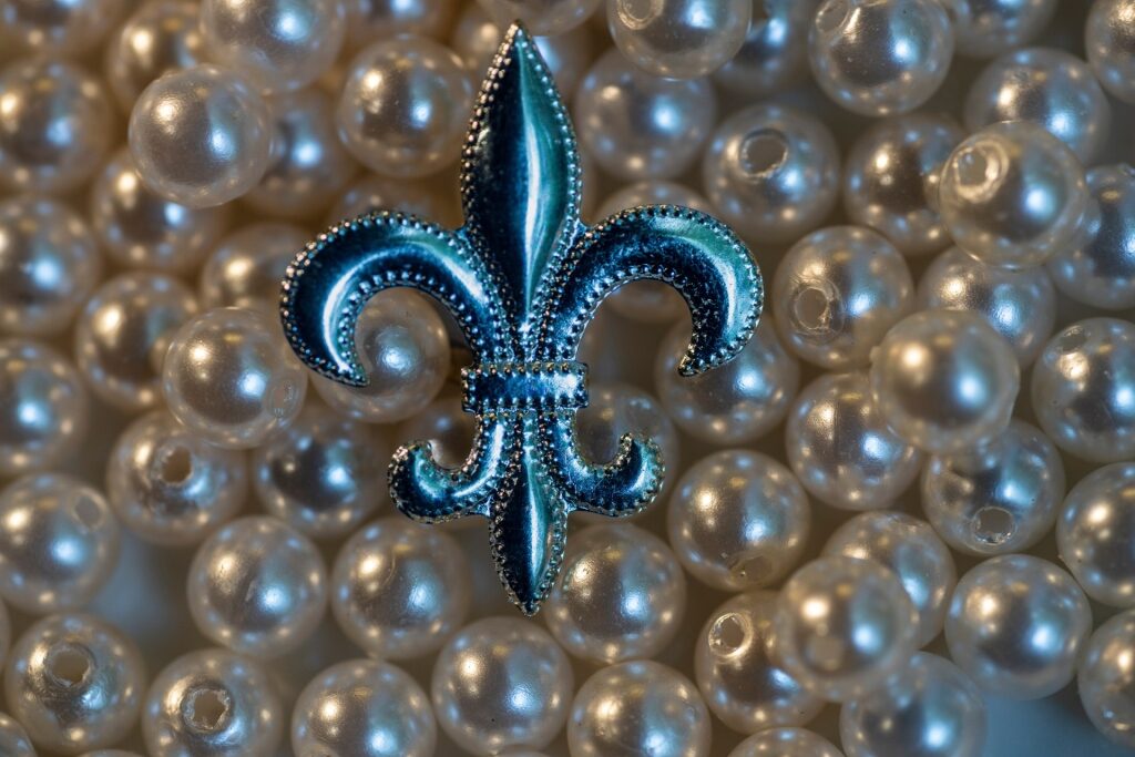 Blue metal fleur-de-lis brooch displayed on a background of faux pearls