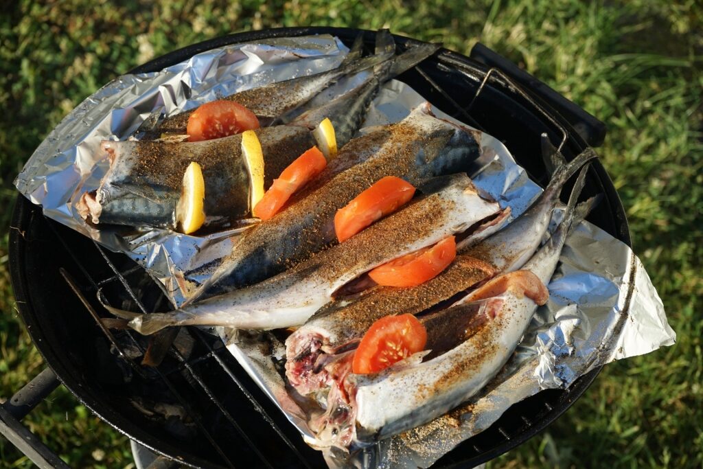 Fresh mackerel seasoned with lemon and tomatoes on an outdoor grill