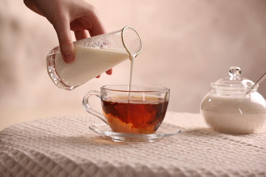 Woman pouring milk into a cup of aromatic tea at a table