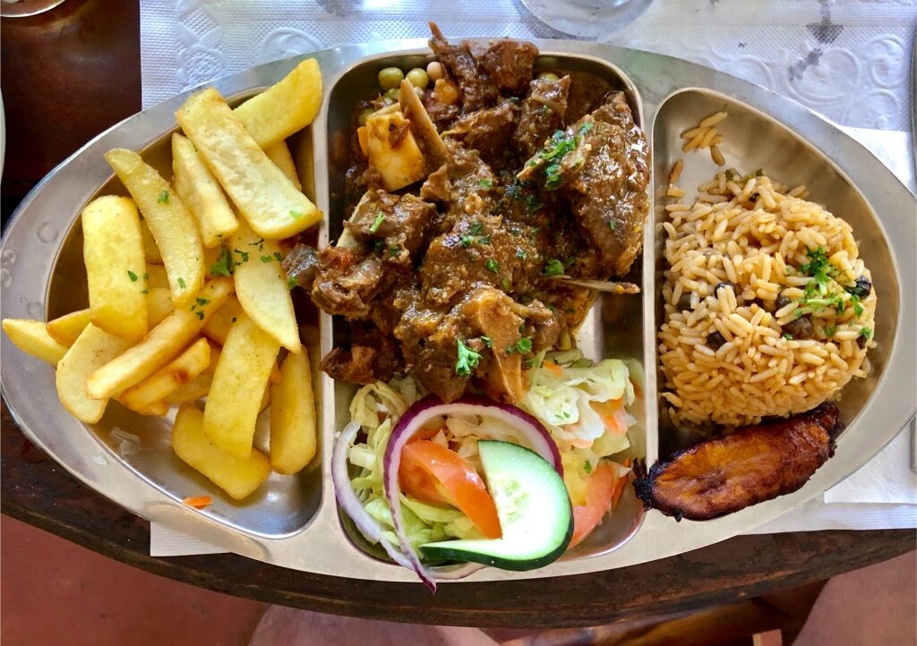 Caribbean goat stew served with French fries and rice and beans