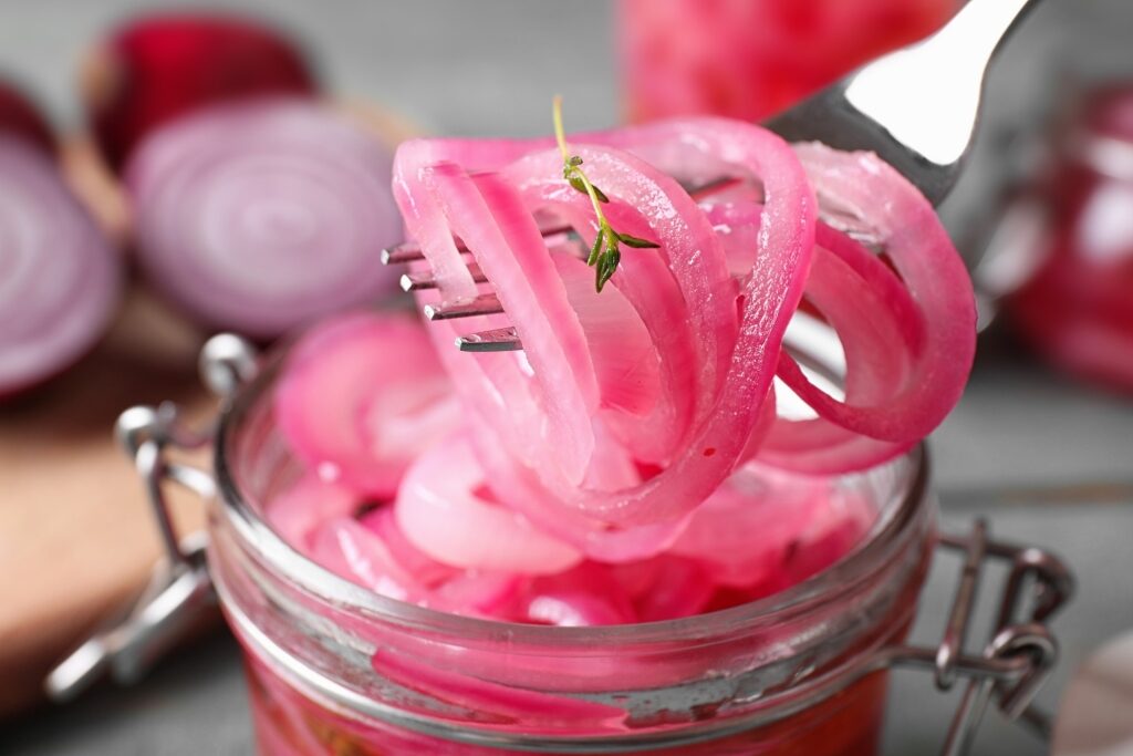 Close-up forkful of pickled onions held over a jar