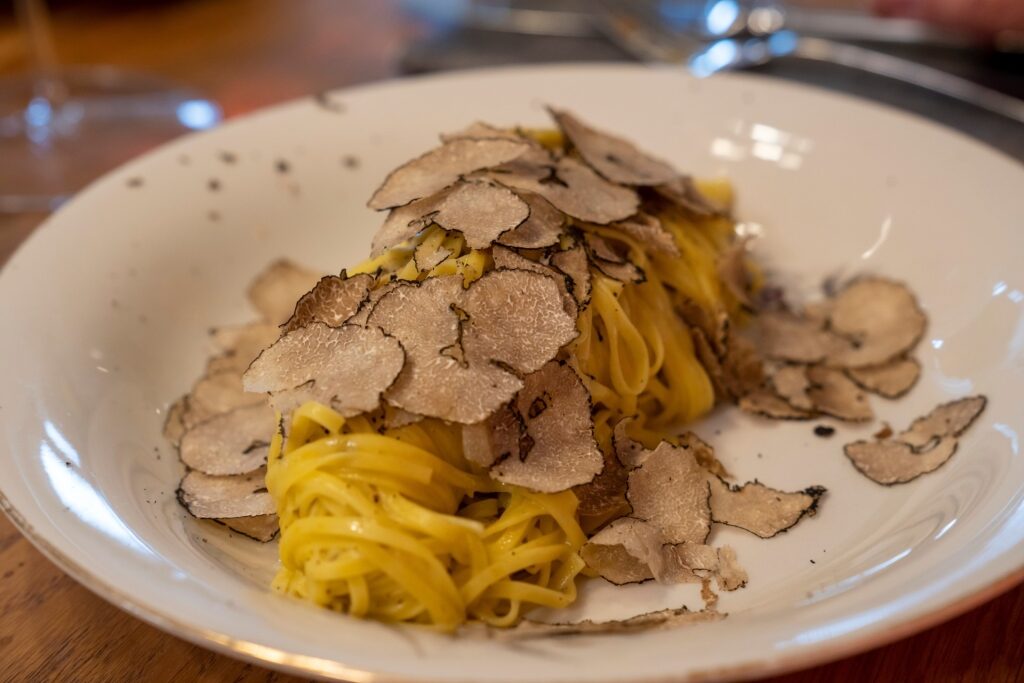 Tagliatelle pasta topped with shaved truffles on a white plate
