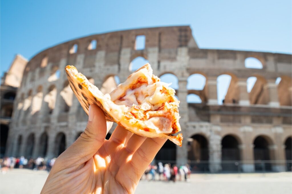 Hand holding a slice of Italian pizza with the Colosseum in the background