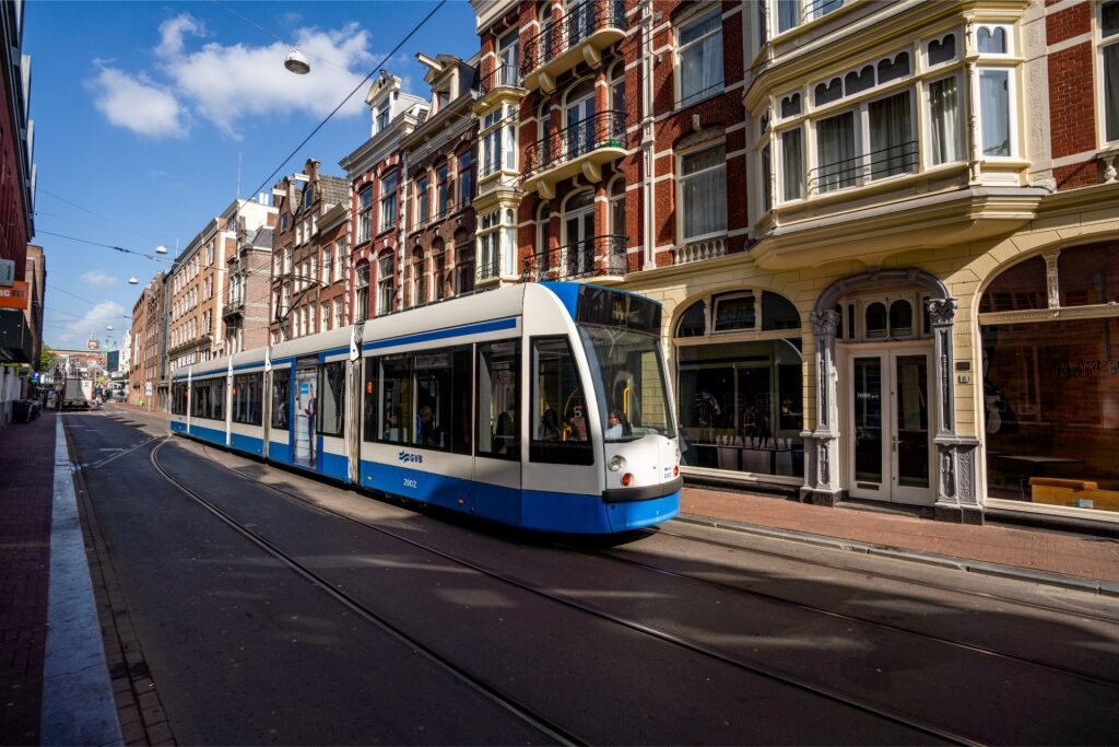 Blue-and-white Amsterdam tram moving through a city street lined with buildings