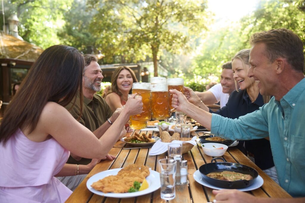 Tourists toasting beer steins in an outdoor beer garden in Austria