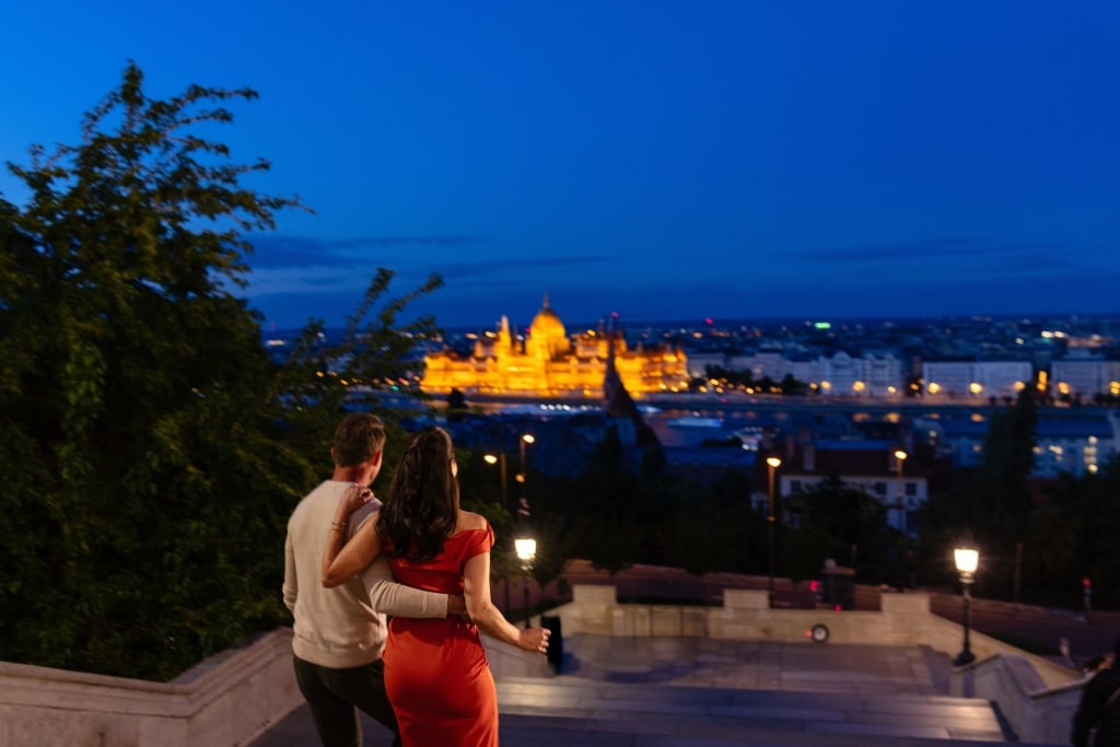 Illuminated golden Budapest Parliament Building frames a couple enjoying a nighttime scenic walk