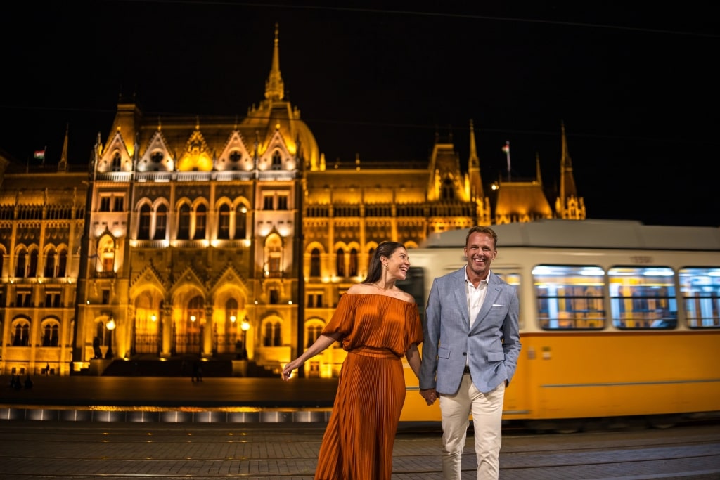 Happy couple strolls, foregrounding the magnificent neo-Gothic Budapest Parliament Building. 