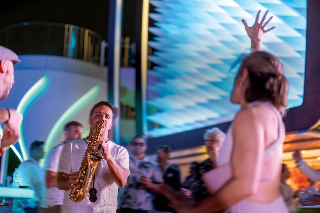 Energetic cruise passengers dancing together inside a vibrant open-air ship nightclub.