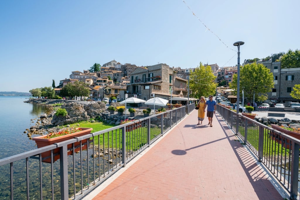 Smiling couple embraces foreground overlooking scenic lakeside Anguillara Sabazia hillside town
