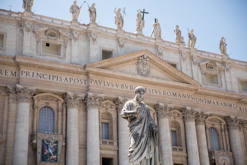 Majestic Saint Peter statue stands foreground framing St. Peter’s Basilica ornate stone façade
