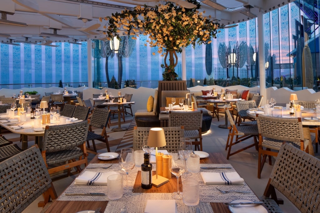 Sophisticated indoor cruise ship restaurant showcasing woven wicker chairs flanking elegant set dining tables.