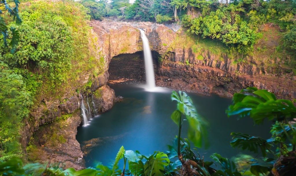 Majestic Hilo Rainbow Falls cascading powerfully into a deep blue tropical volcanic basin pool.