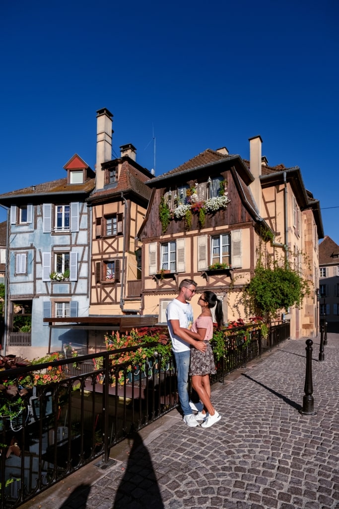 Affectionate couple exploring historic Strasbourg cobblestone pathways facing charming half-timbered canal architecture.