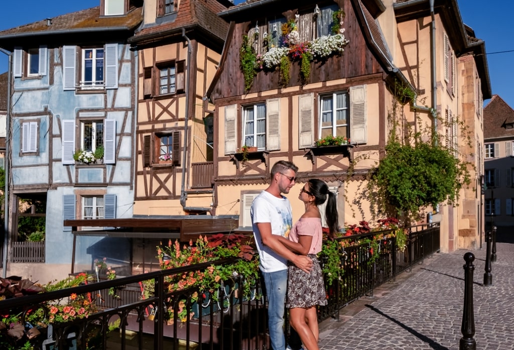 Affectionate couple exploring historic Strasbourg cobblestone pathways facing charming half-timbered canal architecture.