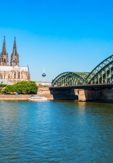 Expansive green Hohenzollern Bridge and Cologne Cathedral twin spires gracing the wide sunlit Rhine River.