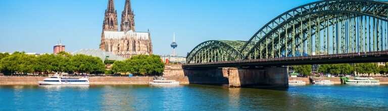 Expansive green Hohenzollern Bridge and Cologne Cathedral twin spires gracing the wide sunlit Rhine River.