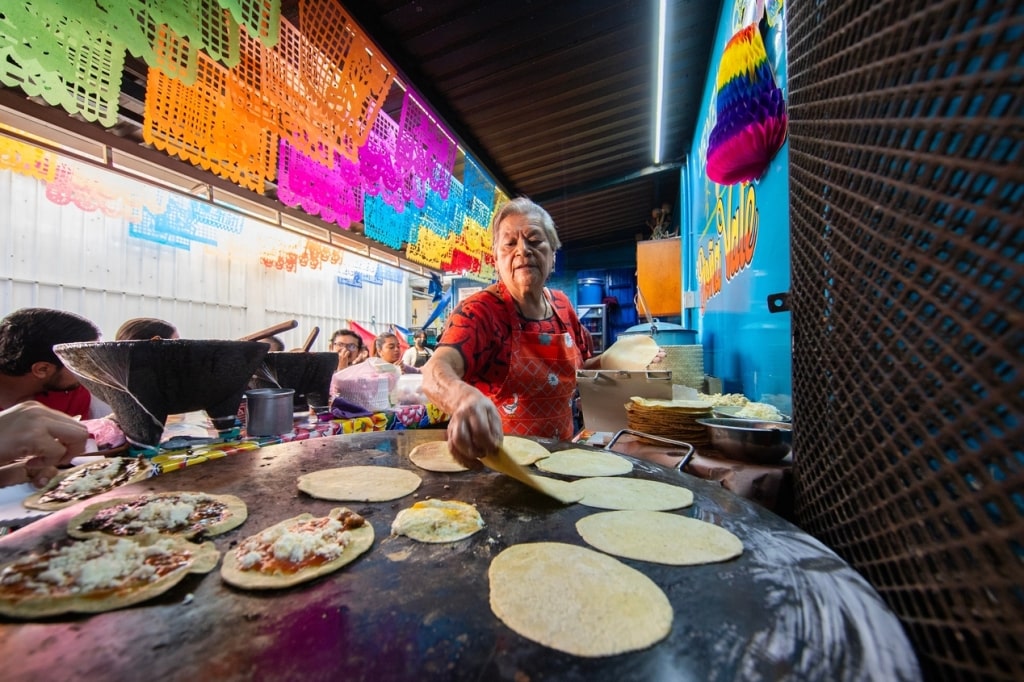 A Mexican woman prepares fresh corn tortillas at a bustling Mexican food stall