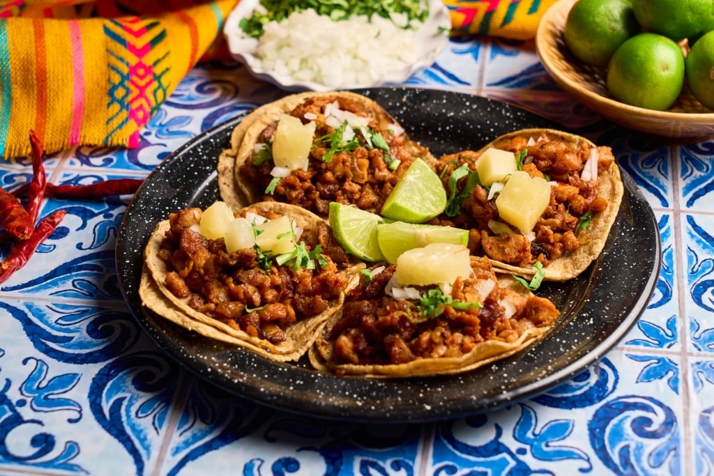 Four tacos al pastor featuring seasoned pork, fresh pineapple chunks, diced onions, and chopped cilantro